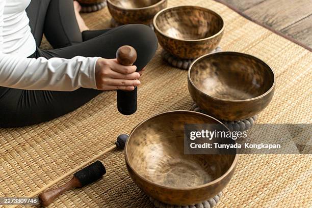 close up of woman's hand practicing sound bath meditation with tibetan singing bowl surrounded by peaceful natural scenery at home, inner peace and nervous system regulation for wellness lifestyle. - music therapy stock pictures, royalty-free photos & images