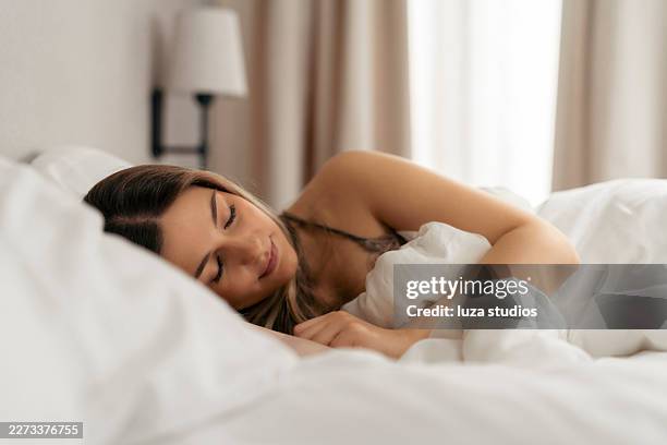 young woman sleeping peacefully in bed under white sheets in a cozy bright bedroom - lying on side stock pictures, royalty-free photos & images