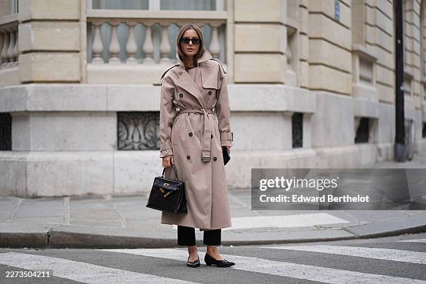 Diane Batoukina wears long straight brown hair, black sunglasses by Kaleos, a beige belted trench coat by Camilla and Marc, black pants by Mango, a...