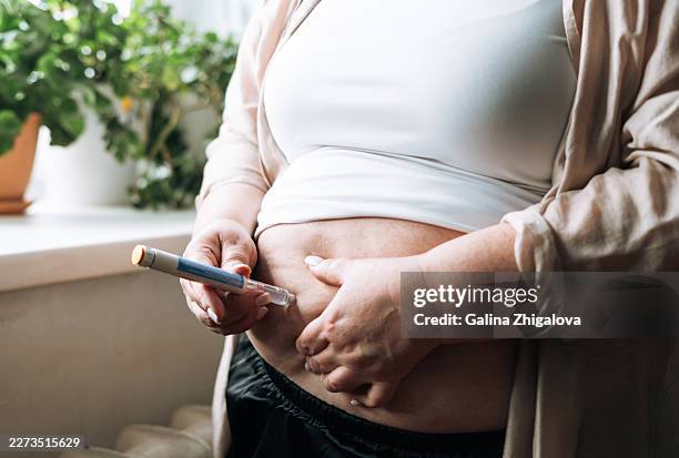 overweight woman self-administering a weight loss injection with a pen injector at home, depicting personal glp-1 therapy and obesity treatment routine - peptide stock pictures, royalty-free photos & images