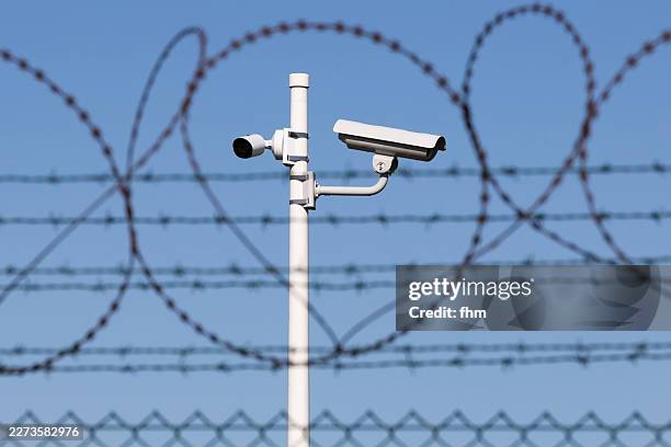 surveillance and security cameras behind a fence with barbed wire - terrorism stock pictures, royalty-free photos & images
