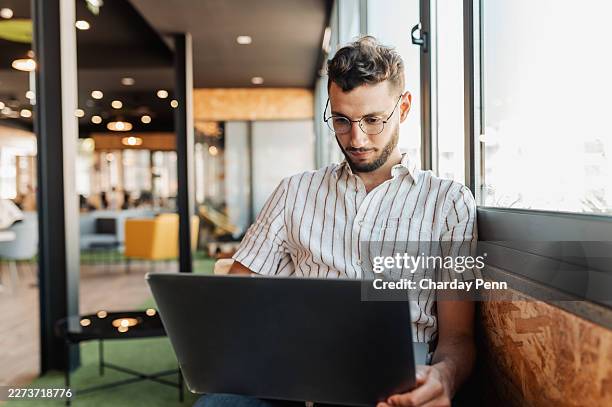 junger unternehmer arbeitet am laptop in einem modernen coworking-space am fenster - lässig schicker stil stock-fotos und bilder