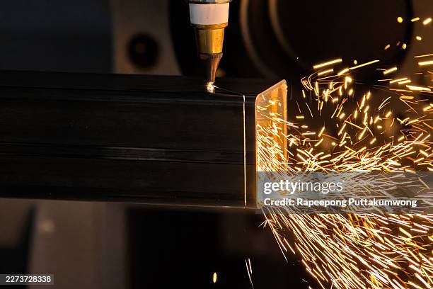 precision industrial fiber laser cutting machine slicing through a heavy steel square tube with golden sparks - laser engraving stock pictures, royalty-free photos & images