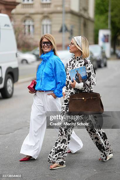 Julia Kammerer is seen wearing a white and brown cow print satin zip up track jacket with a high collar, white ribbed cuffs, a three white side...