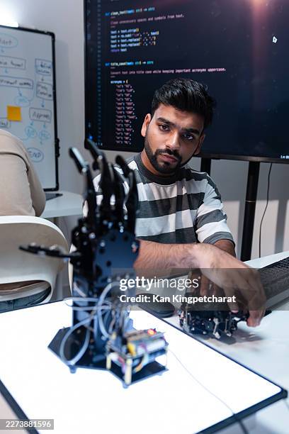 engineer building robotics software with robotic hand prototype on desk during artificial intelligence development session. - robot prototype stock pictures, royalty-free photos & images