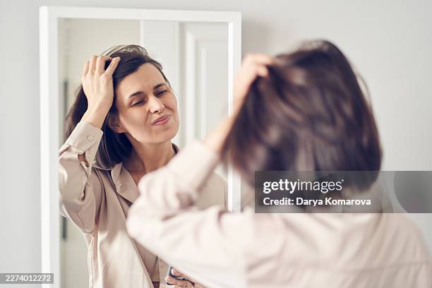 middle-aged woman checking her hair and smiling at her reflection in a bedroom mirror - backstage bildbanksfoton och bilder