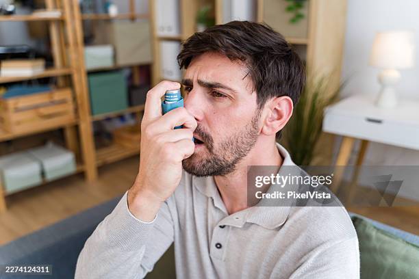 man using inhaler for asthma breathing difficulty at home - difficult breathing stock pictures, royalty-free photos & images