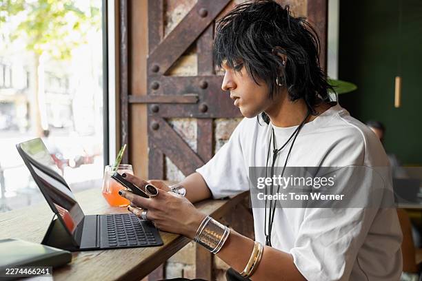 creative young man using smartphone and tablet while sitting at cafe bar - digital native stock pictures, royalty-free photos & images