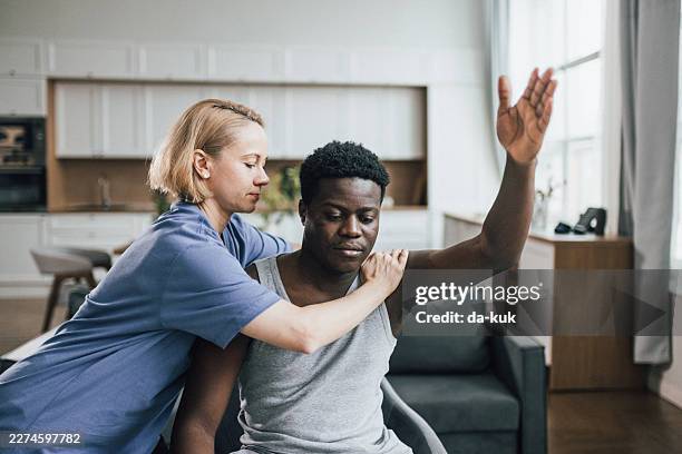 physiotherapist assisting man with shoulder stretch during home rehabilitation session - homeostasis stock pictures, royalty-free photos & images
