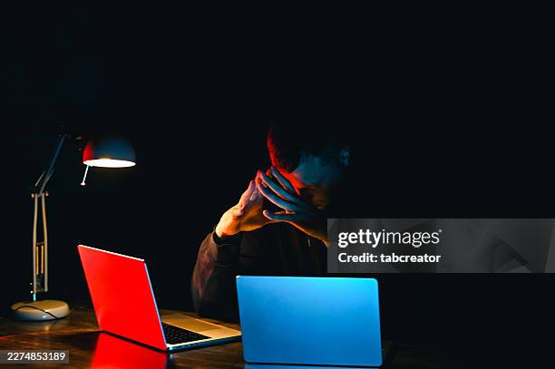 hacker concentrating on laptops in dark room with cybersecurity issues - trade secrets stock pictures, royalty-free photos & images