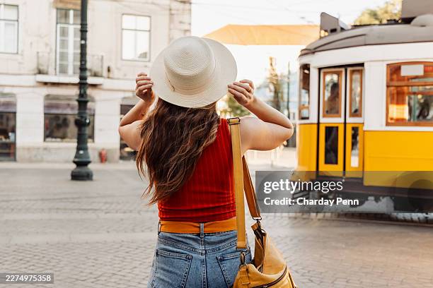 donna con il cappello di paglia che aspetta il tram giallo in una affascinante strada della città europea - borsa a tracolla foto e immagini stock