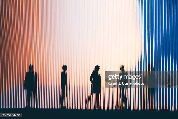 silhouetted figures of people standing behind a vibrant, vertically ribbed screen with warm orange and cool blue lighting. - human rights stock pictures, royalty-free photos & images