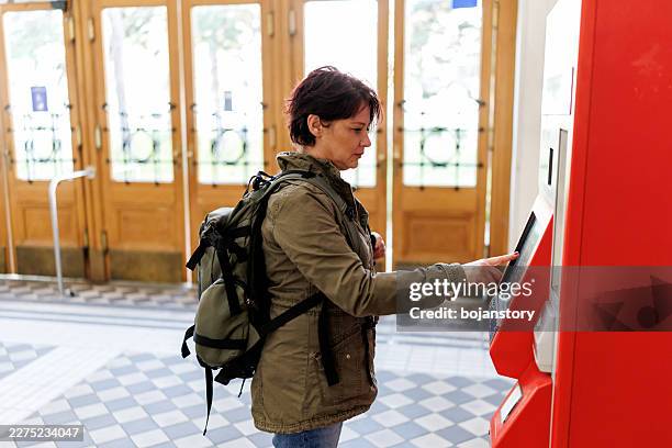 female passenger with backpack buying train ticket at self-service machine - self service stock pictures, royalty-free photos & images