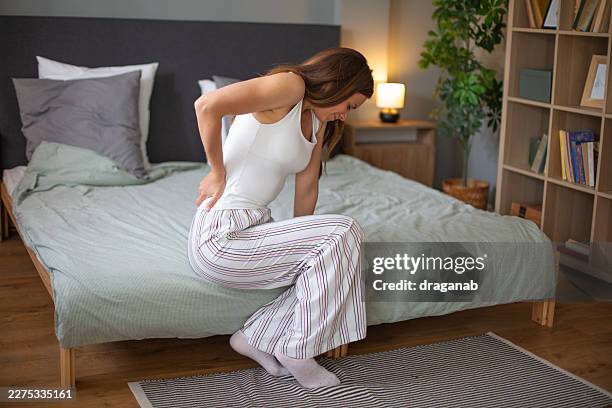 mujer con dolor de espalda sentada en la cama en casa - fibromialgia fotografías e imágenes de stock