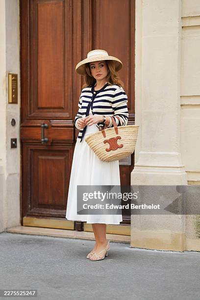 Merve Gorgoz wears a beige wide-brim hat by Rose Cherie, long wavy light brown hair, a navy blue and white striped knit jacket by Karen Millen, a...
