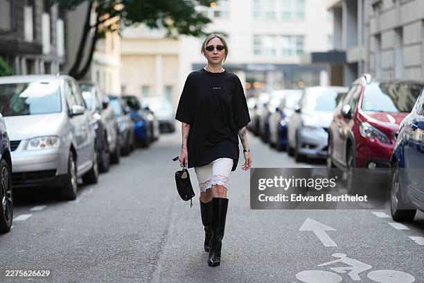 Emy Venturini wears blonde hair tied back in a low bun with loose face-framing strands, black oval Balenciaga sunglasses with dark lenses, natural...
