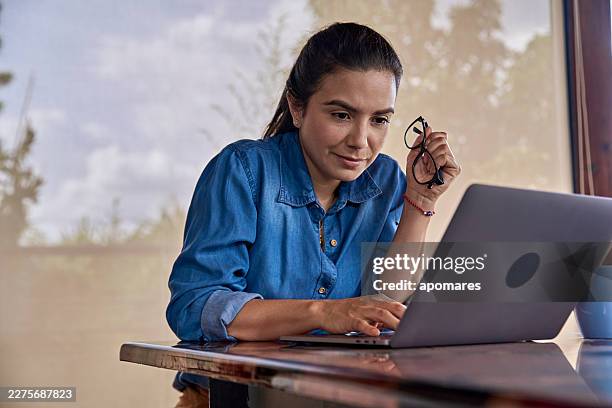 hispanische frau, die im homeoffice an ihrem laptop arbeitet. - websurfen stock-fotos und bilder