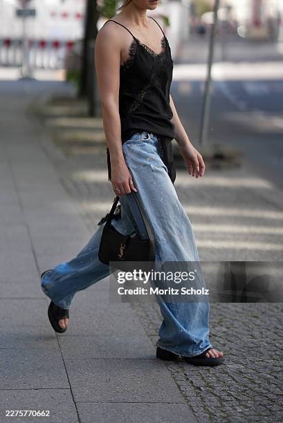 Sophia Geiss is seen wearing a black satin camisole slip top with thin spaghetti straps, a V-neckline with black lace trim, and an asymmetric...