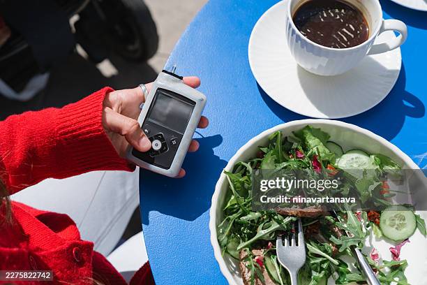 overhead view of a diabetic woman sitting at a table with a cup of black coffee and roast beef salad using an insulin pump - hypoglycemia stock pictures, royalty-free photos & images
