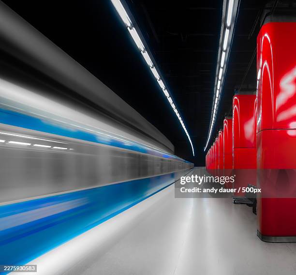 subway train in motion on a modern, empty platform with red architectural elements and bright lights - underground train stock pictures, royalty-free photos & images