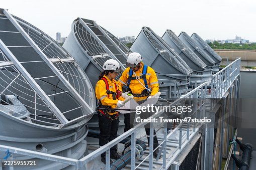 Construction workers using safety harnesses while performing a routine chiller inspection on a high-rise building Construction workers using safety harnesses while performing a routine chiller inspection on a high-rise building