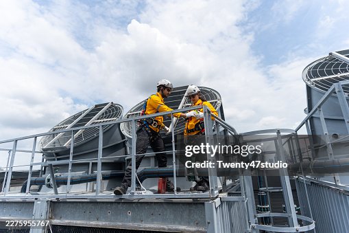 Construction workers using safety harnesses while performing a routine chiller inspection on a high-rise building Construction workers using safety harnesses while performing a routine chiller inspection on a high-rise building