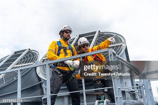 Construction workers using safety harnesses while performing a routine chiller inspection on a high-rise building Construction workers using safety harnesses while performing a routine chiller inspection on a high-rise building