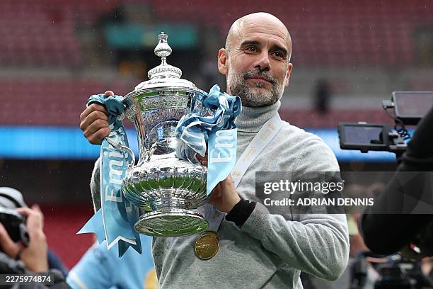 Manchester City's Spanish manager Pep Guardiola poses with the trophy on the pitch after the English FA Cup final football match between Chelsea and...