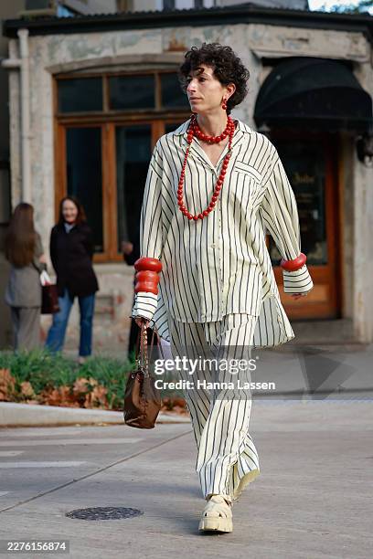 Guest wearing red beaded necklace, matching earrings and bangles, ivory pin-stripped shirt and matching pants, brown Prada bag and ivory Prada shoes...