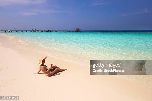 happy woman drinking juice while relaxing in sand on the beach. - sun tan stock pictures, royalty-free photos & images