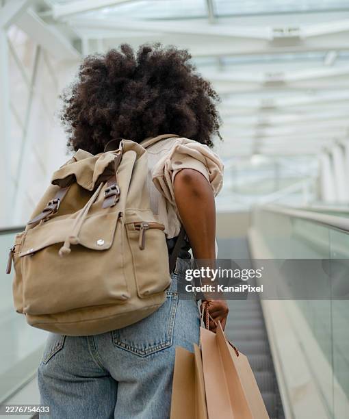 mujer de compras, montando una escalera mecánica en un centro comercial moderno - cabello afro fotografías e imágenes de stock