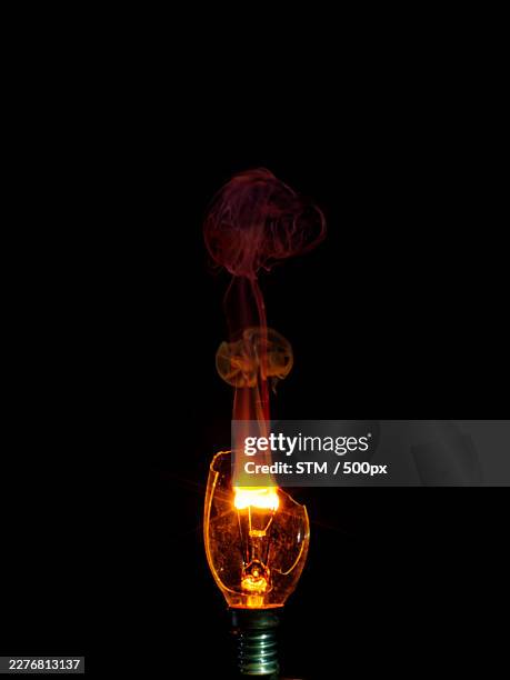 exploding light bulb with glowing filament and smoke on a black background - exploding lightbulb stock pictures, royalty-free photos & images