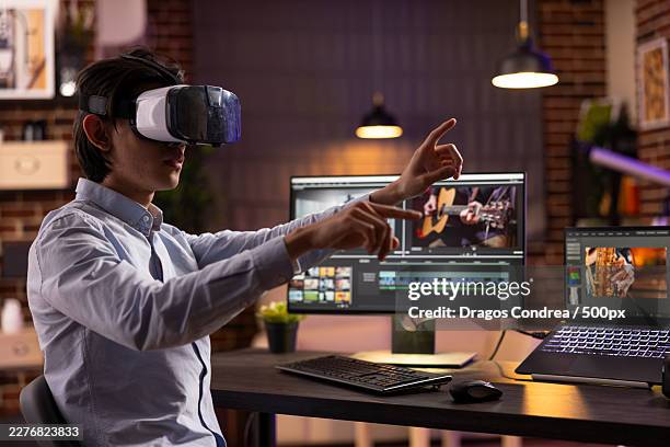 young man in vr headset interacting with virtual elements while video editing at night - oficio de diseño fotografías e imágenes de stock