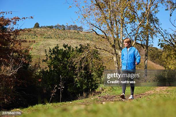 woman walking on a countryside trail in a blue jacket during a sunny autumn day - foothills stock pictures, royalty-free photos & images