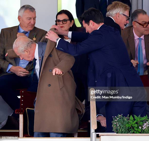Lieutenant Colonel Jonny Thompson helps King Charles III put on his overcoat as they watch 'Azerbaijan - Land of Fire', the 'DAKS Pony Club Mounted...
