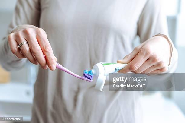 woman squeezing toothpaste onto a toothbrush during morning oral hygiene routine in bright bathroom - squeezing toothpaste stock pictures, royalty-free photos & images