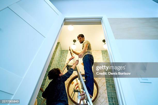 couple on ladder doing home improvement and lighting repair - dedicação imagens e fotografias de stock