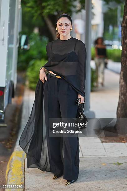 Yayis Villarreal is seen wearing their brown hair in a high ponytail, gold ribbed clip-on earrings, a black sheer long-sleeved tunic top, a black...