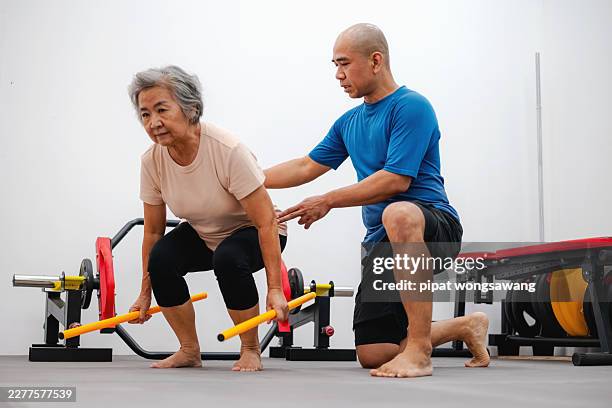elderly woman practicing deadlift exercise with trainer support - fisiologia imagens e fotografias de stock