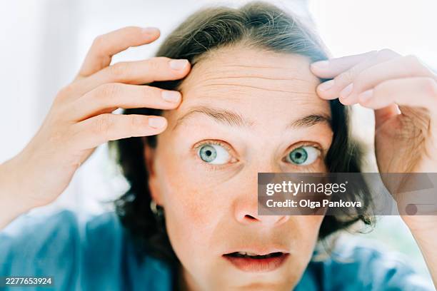 mid adult woman checking wrinkles on forehead - regarder fixement photos et images de collection