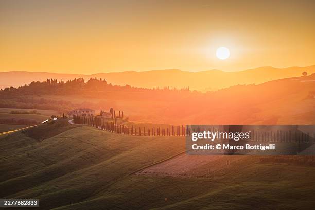 golden sunset over rolling hills with a cypress alley and farmhouse, val d'orcia, tuscany - puesta de sol romántica fotografías e imágenes de stock