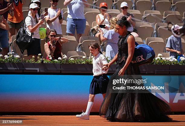 Japan's Naomi Osaka holds a mascots hand as she walks on Court Suzanne-Lenglen to player her women's singles match against Germany's Laura Siegemund...