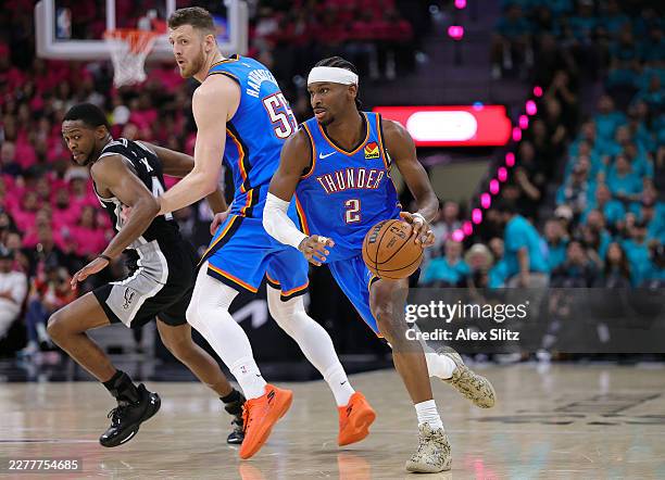 Shai Gilgeous-Alexander of the Oklahoma City Thunder dribbles around Isaiah Hartenstein against De'aaron Fox of the San Antonio Spurs during the...