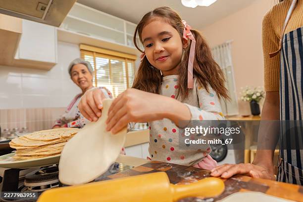 young girl with long brown hair and pink ribbons making homemade chapati in a cozy kitchen with her family. - roti stock pictures, royalty-free photos & images