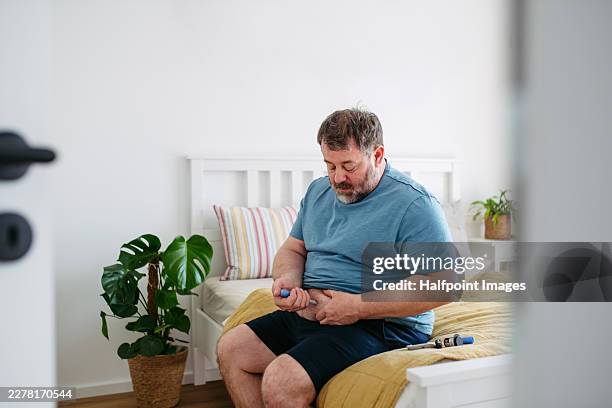 diabetic man injecting insulin into abdomen, sitting on bed. - hypoglycemia stock pictures, royalty-free photos & images