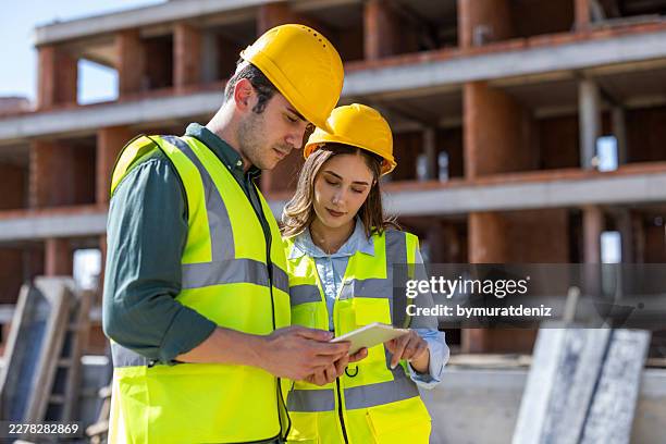 two engineers checking project data on digital tablet at construction site - construction consulting stock pictures, royalty-free photos & images