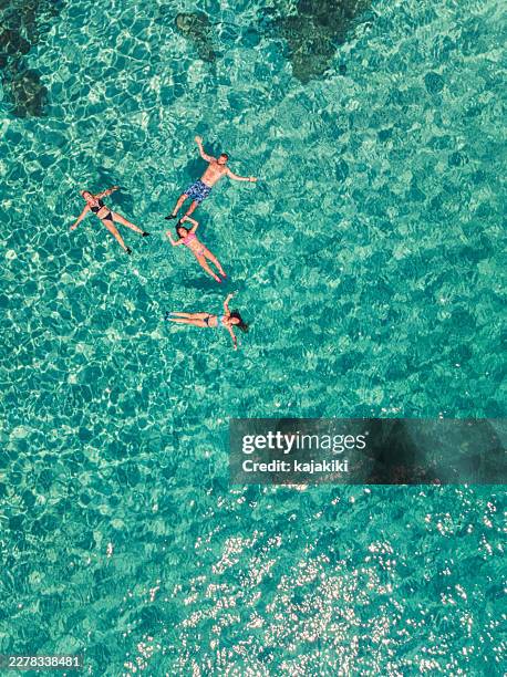 aerial view of a young family floating and swimming on a beautiful beach on a greek island - floating on water stock pictures, royalty-free photos & images