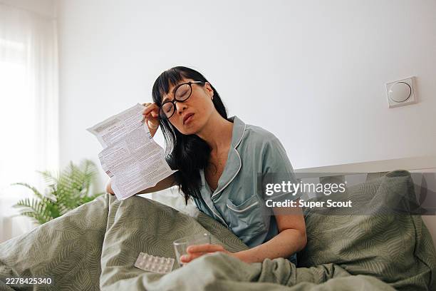 japanese woman reading hrt instructions with glass of water on bed - hormone therapy stock pictures, royalty-free photos & images