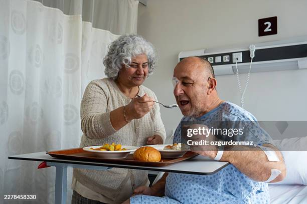 moglie premurosa che aiuta il marito sorridente a mangiare in ospedale - rapporto medico paziente foto e immagini stock