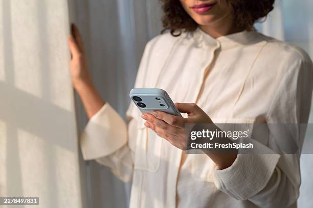 woman using smartphone near curtain in natural light - mensagem com foto imagens e fotografias de stock